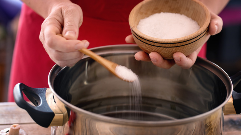 A person adding salt to a pot of water.