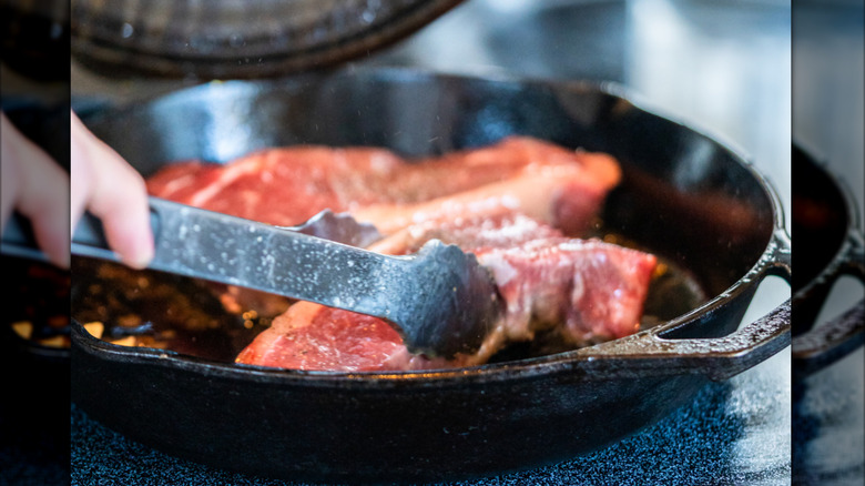 A chef preparing a steak in a cast iron skillet