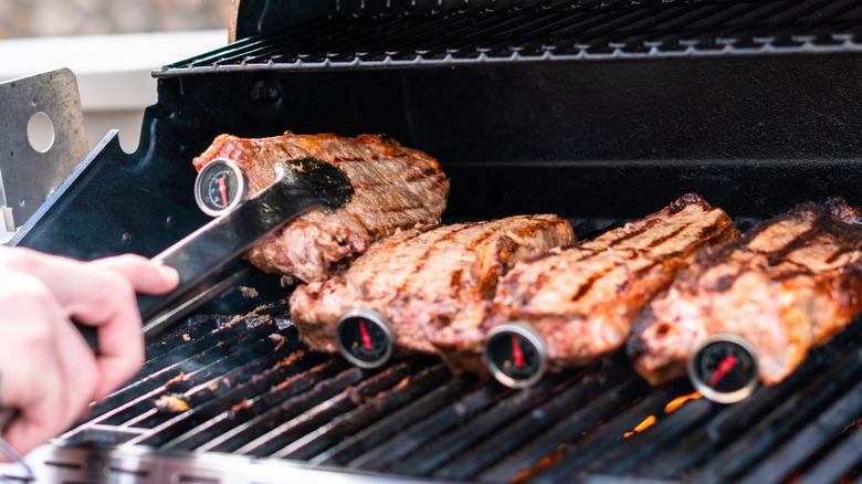 Four New York strip steaks on a grill with thermometers in them