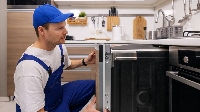 A person in blue work clothes installs a large kitchen appliance.