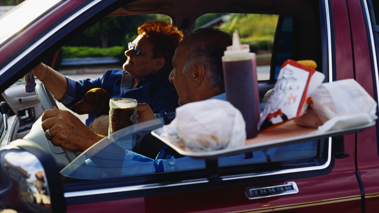A couple in a car receiving a plastic tray with food and drinks from a drive-thru.