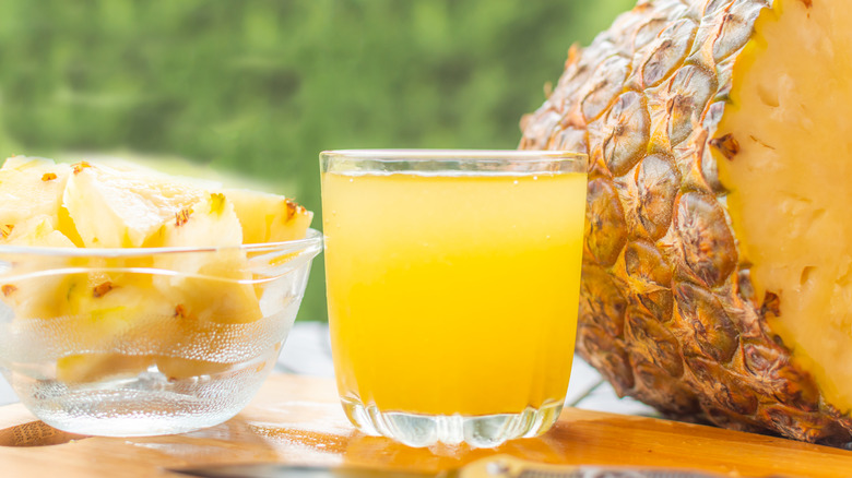 A glass of pineapple juice is styled with cubed and halved pineapples.