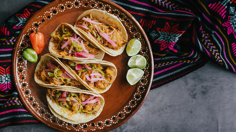 Decorative plate of four tacos with small whole chili peppers and a few lime wedges.