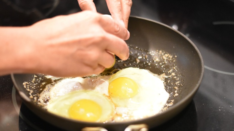 A person cracking eggs into a hot skillet