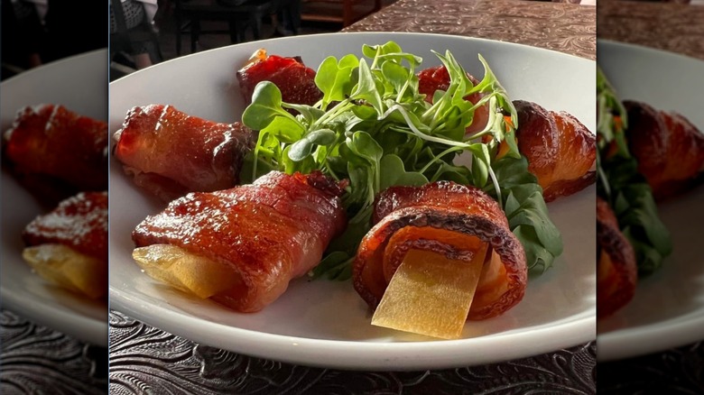 Pickled watermelon rinds wrapped in bacon on white plate.