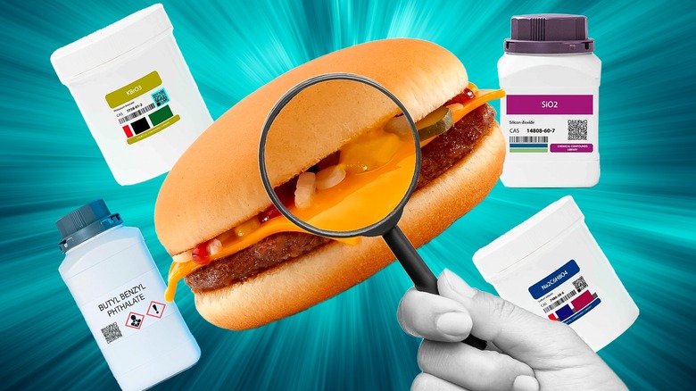 A hand holding a magnifying glass over a cheeseburger with chemical containers in the background