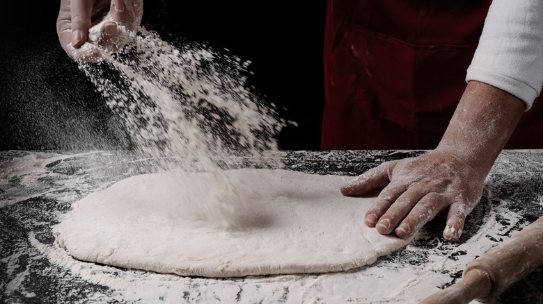 Person sprinkles flour onto pizza dough