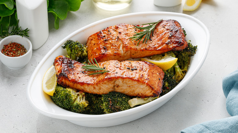 Baking dish with broccoli, lemon slices, and two cooked salmon fillets topped with rosemary sprigs