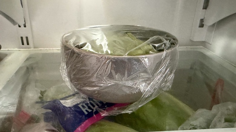 Avocado crema in plastic-covered bowl in refrigerator