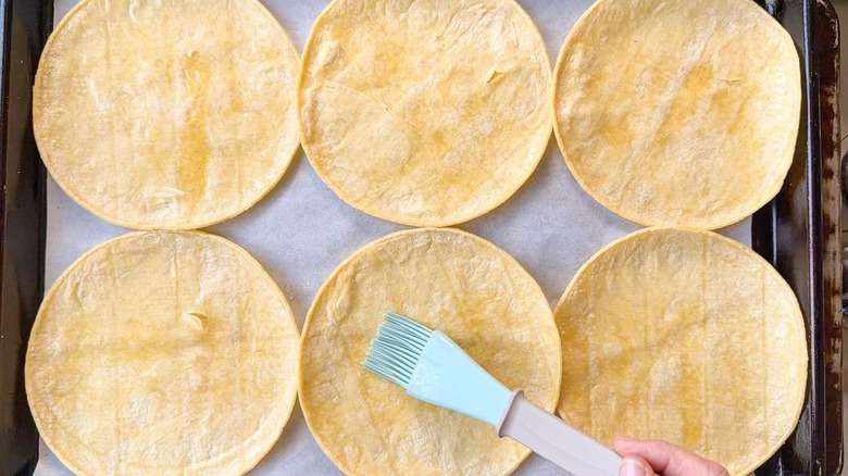 Brushing avocado oil onto corn tortillas on parchment-lined sheet pan