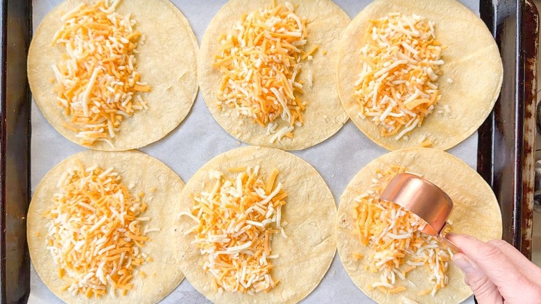 Filling corn tortillas on parchment-lined sheet pan with shredded cheese