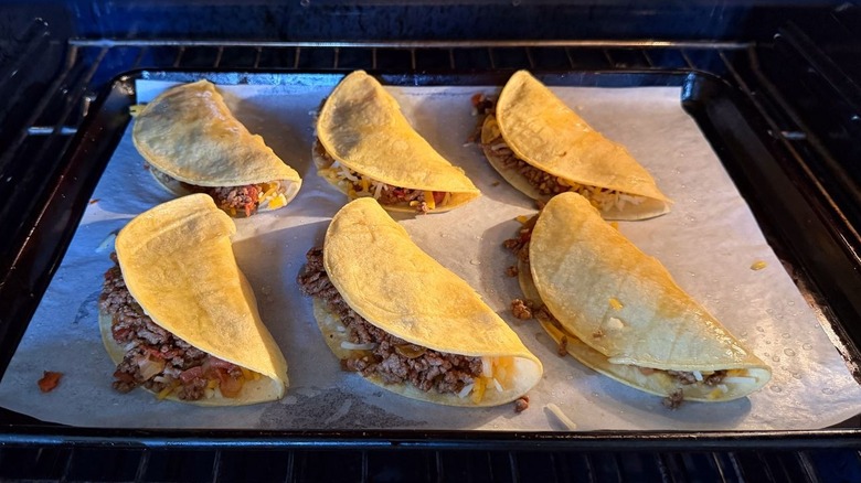 Beef tacos baking on parchment-lined baking sheet in oven