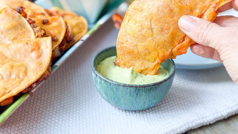 Dipping baked crispy beef taco into bowl of avocado crema