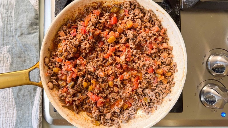 Browned ground beef, red salsa, and golden raisins in skillet on stovetop
