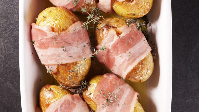 Potatoes wrapped in raw bacon with herbs.