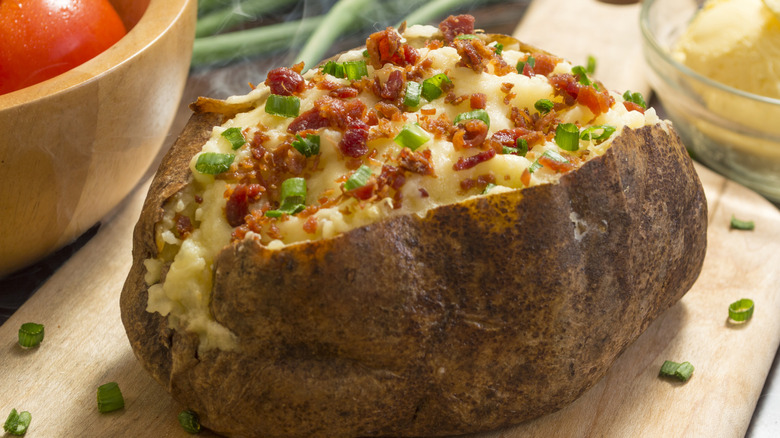 A hot baked potato with bacon bits and chopped scallions.