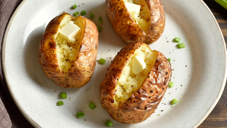 Baked potatoes on a dish with butter and chopped herbs