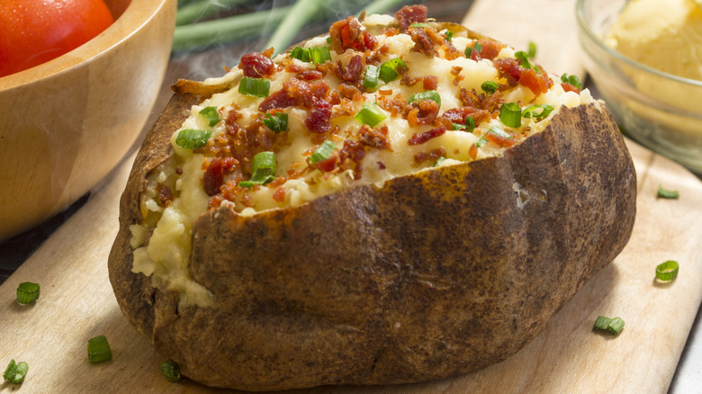 Baked potato on wooden plank with bacon bits and chives
