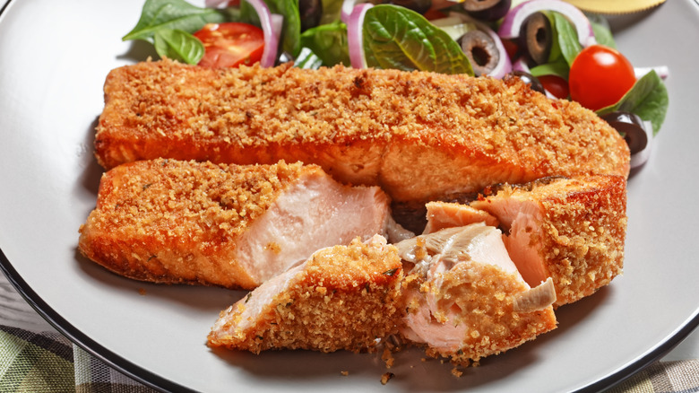 Crusted salmon is plated with a side salad.