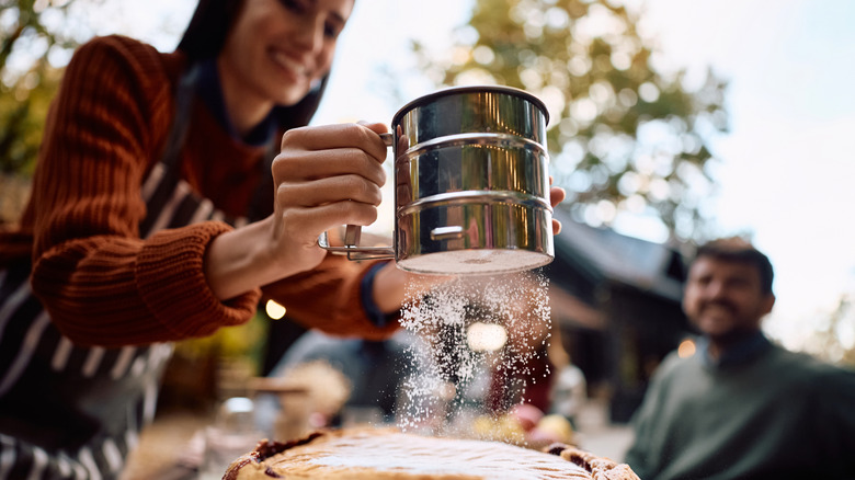 Close up of woman sifting powdered sugar on pie.