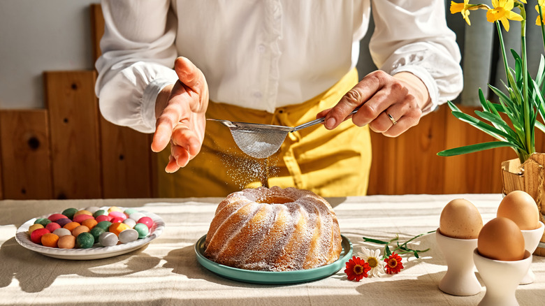Hands sprinkling cake with powdered sugar through sieve.