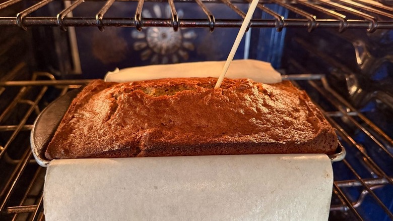 Wooden tester inserted into bakery-worthy banana bread in loaf pan in oven
