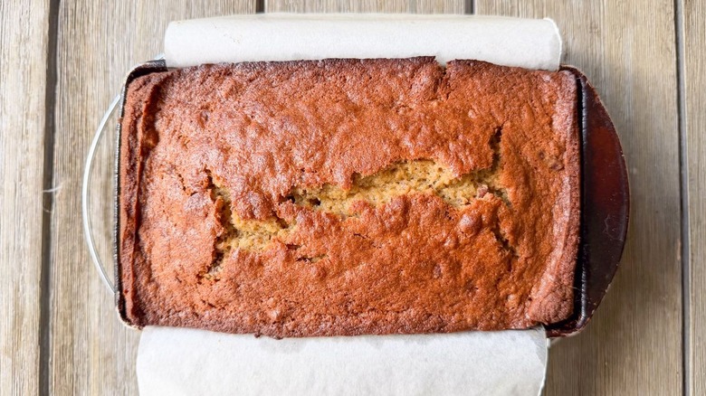 Bakery-worthy banana bread cooling in parchment-lined loaf pan on table