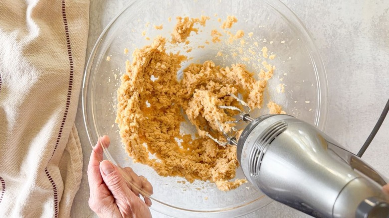 Creaming together butter and brown sugar with hand-held mixer in glass bowl