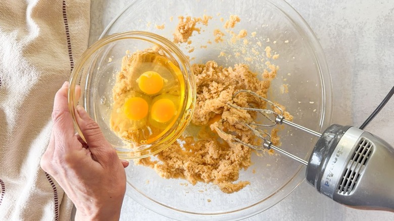 Adding eggs to brown sugar and butter in glass bowl with hand mixer