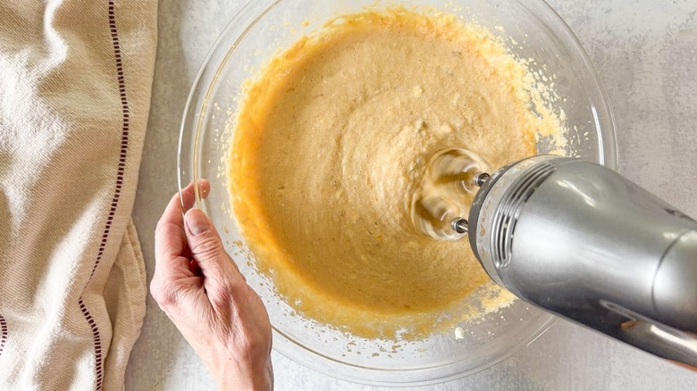 Stirring banana bread mixture with hand mixer in glass bowl