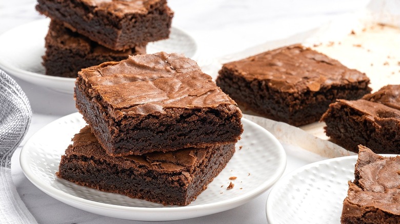 Chocolate brownies stacked on small white plates.
