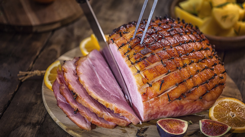 Knife carving off slices of glazed ham