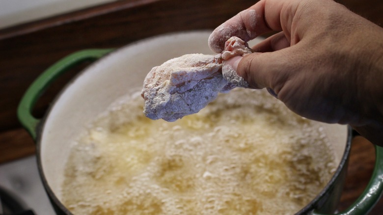 dropping chicken wing into pot of oil