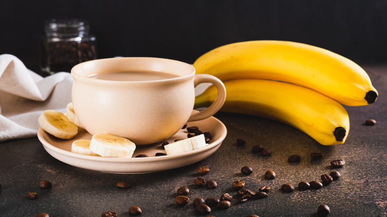 Cup of cold banana coffee with bananas and coffee beans in background