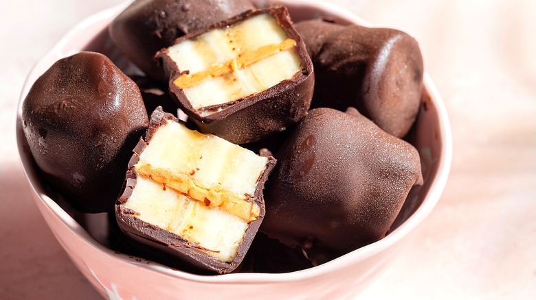 Frozen banana and cookie butter sandwich bites coated in chocolate in a pale pink bowl.