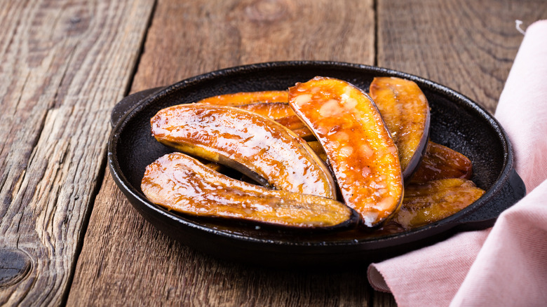 Caramelized bananas in a cast iron pan on a wooden table with a cloth napkin