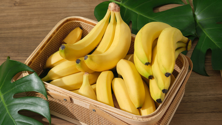 Basket of bananas sitting on a wooden table with banana leaves