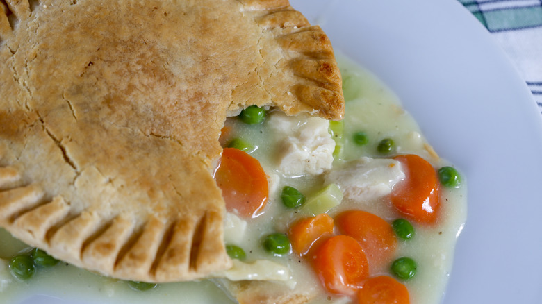 Chicken pot pie with a piece cut out of the crust with chicken, peas, potatoes, and carrots.