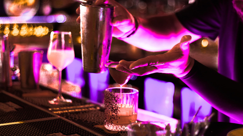 Bartender straining a cocktail into a rocks glass with large ice cube