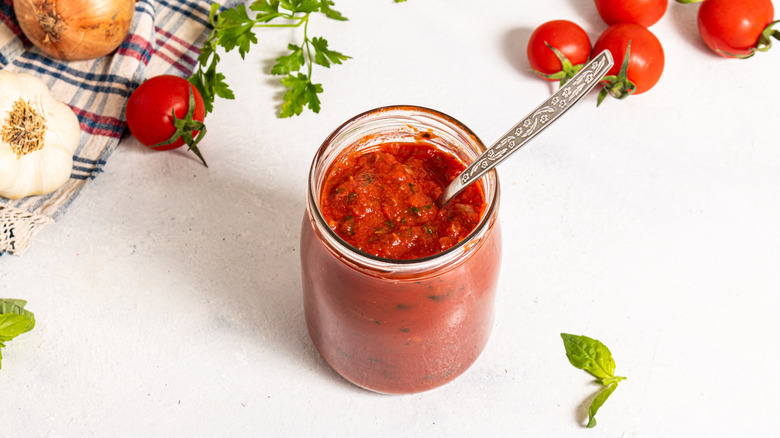 Glass jar with tomato sauce and a spoon inside