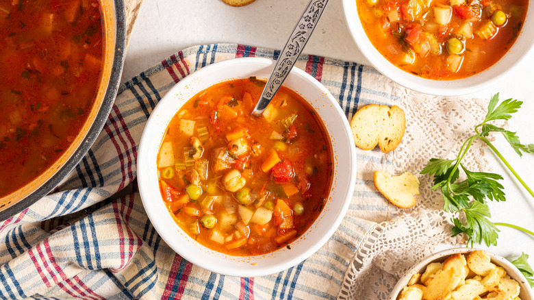 Bowl with tomato and herb vegetable soup over a kitchen towel, and crackers next to the bowl