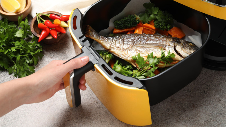 Person holding air fryer basket with a fish inside it.