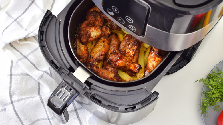 Air fryer with open basket filled with chicken and french fries.