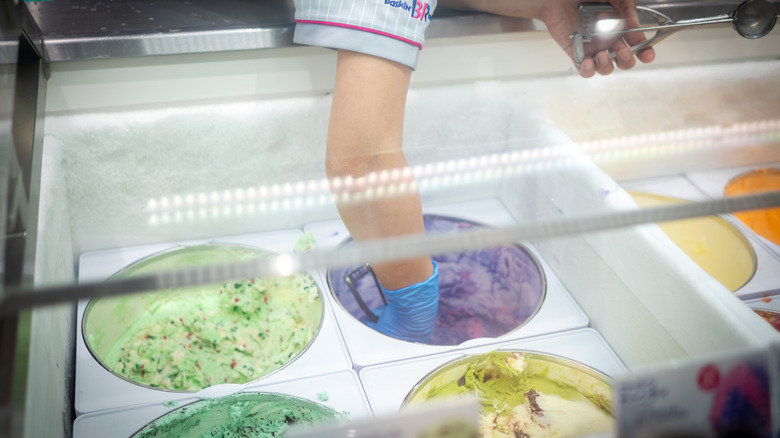 Baskin-Robbins employee scooping out from one of several colorful ice cream tubs
