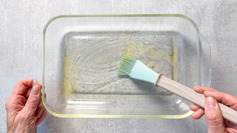 Brushing oil onto the inside of a glass baking dish with pastry brush