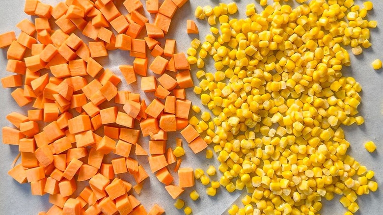 Cubed sweet potatoes and corn kernels on parchment-lined baking sheet