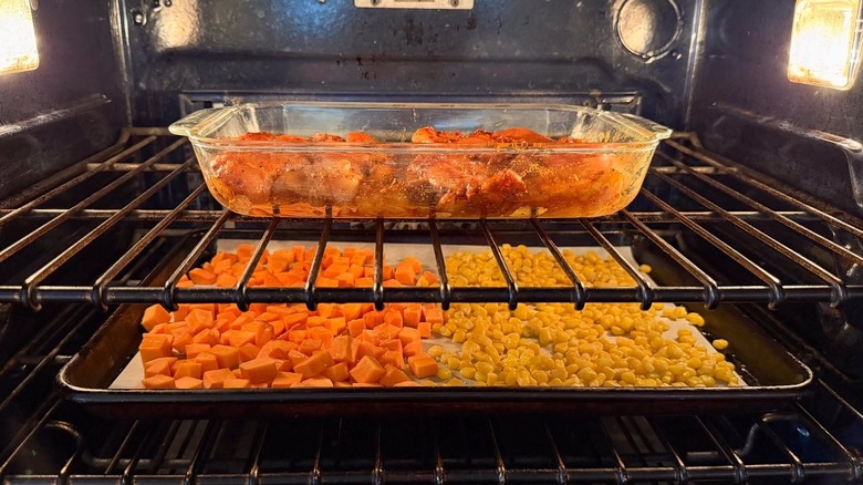 Chicken, sweet potatoes, and corn roasting in pans in oven