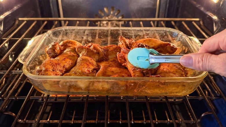 Flipping chicken pieces in baking dish in oven with tongs