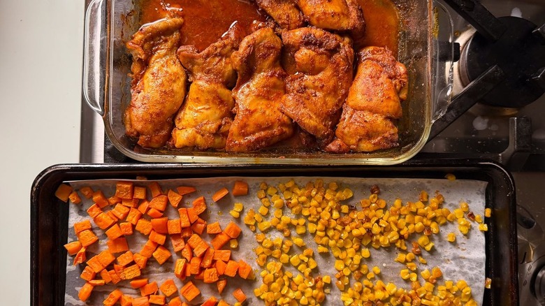 Roasted chicken thighs, sweet potatoes, and corn in baking dishes on stovetop