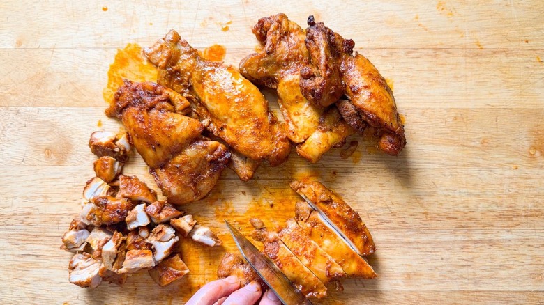 Chopping roasted and dry-rubbed chicken thighs on cutting board